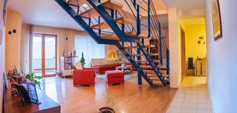 Interiér vily s podlahou s dřevěným dekorem, schodištěm a červenou sedací soupravou.