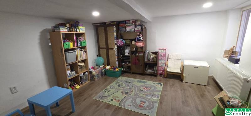 Dětský pokoj v rodinném domě s hračkami, poličkami a koberec na podlaze s dřevěným dekorem.