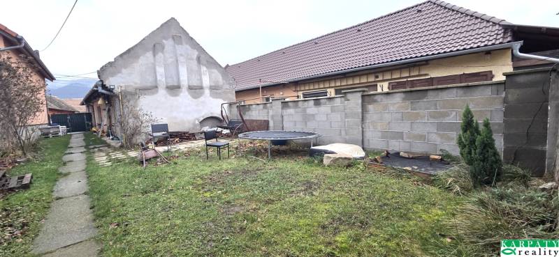 Zahrada u rodinného domu v Dolních Orešanech s betonovým plotem a trampolínou.