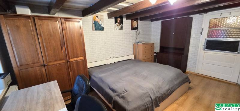 Ložnice v rodinném domě s dřevěným trámovým stropem, nábytkem a dekorativními obrazy.