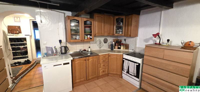 Kuchyně v rodinném domě s dřevěnými skříňkami, spotřebiči a bílou stěnou.