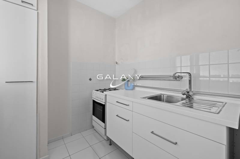 Kuchyně v 1-pokojovém bytě s bílou kuchyňskou linkou a sporákem.