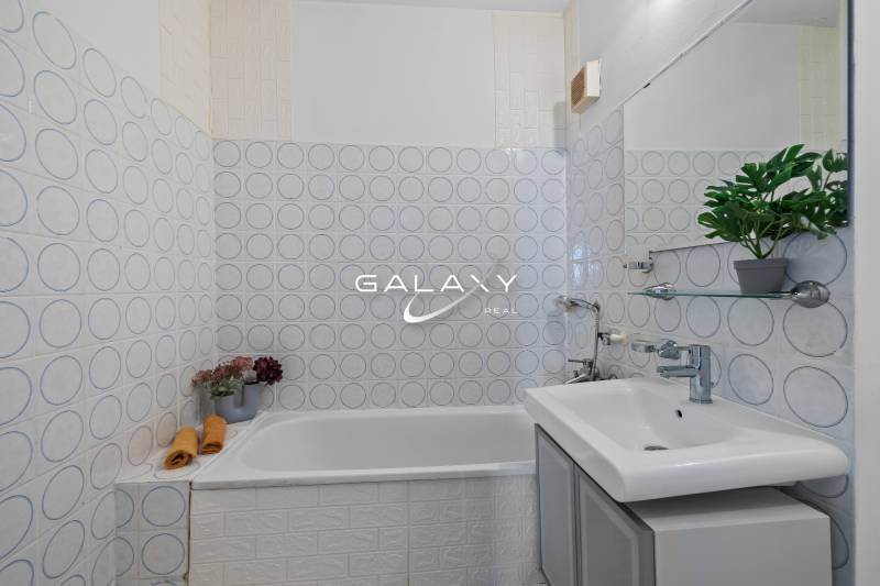 Koupelna s vzorovanými dlaždicemi, vanou a rostlinou v garsonce.