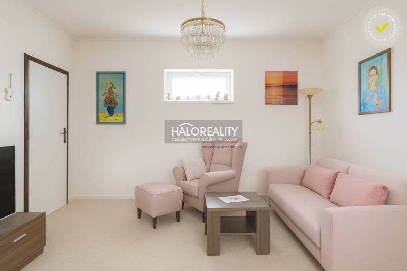 Obývací pokoj s pastelovou sedačkou a křeslem v rodinném domě, dekorativní obrazy na stěnách.