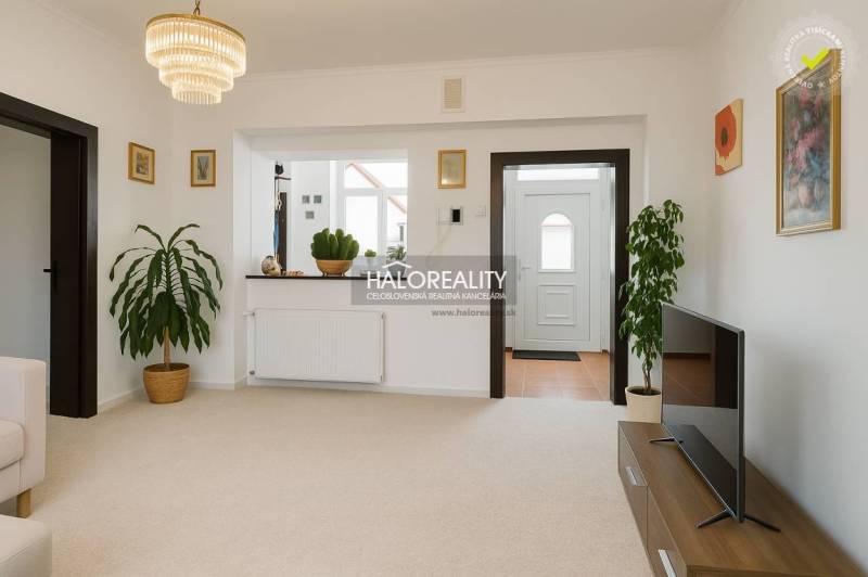 Obývací pokoj v rodinném domě s bílými stěnami, květinami a televizí na stolku.