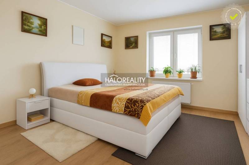 Ložnice v rodinném domě s postelí, nočním stolkem a oknem s pokojovými rostlinami.