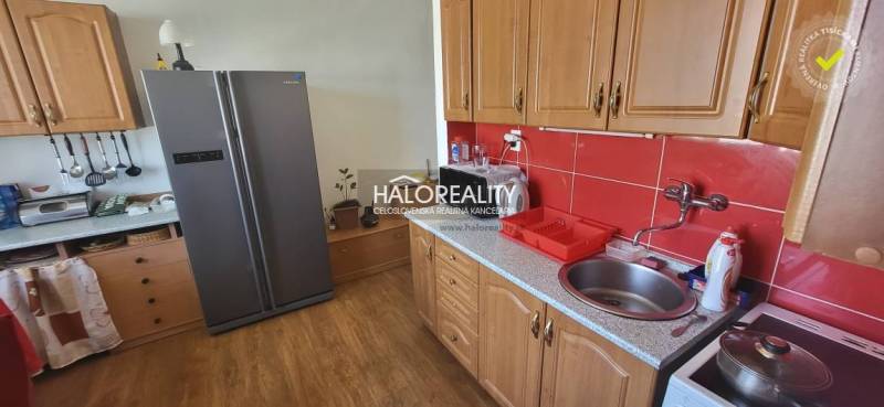 Kuchyně v 1-pokojovém bytě s dřevěnými skříňkami, červenými kachličkami a velkou lednicí.