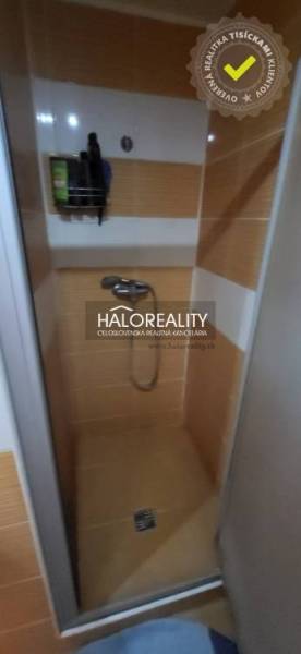 Sprchový kout v 1-pokojovém bytě s oranžovými dlaždicemi a úložným prostorem na stěně.