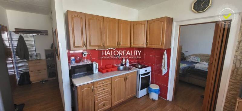 Kuchyně v 1-pokojovém bytě s dřevěnými skříňkami, mikrovlnkou a sporákem.