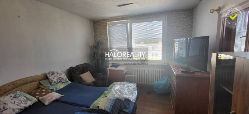 Pokoj v 1-pokojovém bytě s postelí, křeslem, televizí a velkým oknem.