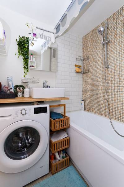 Koupelna v 2-pokojovém bytě s pračkou, vanou a policemi, bílý obklad.