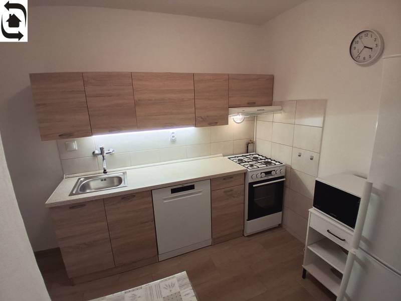 Kuchyně ve 3-pokojovém bytě s linkou, sporákem, myčkou a podlahou s dřevěným dekorem.