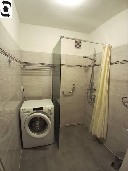 Koupelna se sprchovým koutem, pračkou a světlými obklady ve 3-pokojovém bytě.