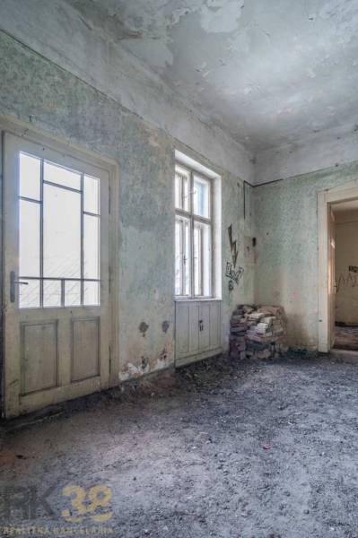 Interiér budovy s poškozenými stěnami, dveřmi a okny, cihly na podlaze.