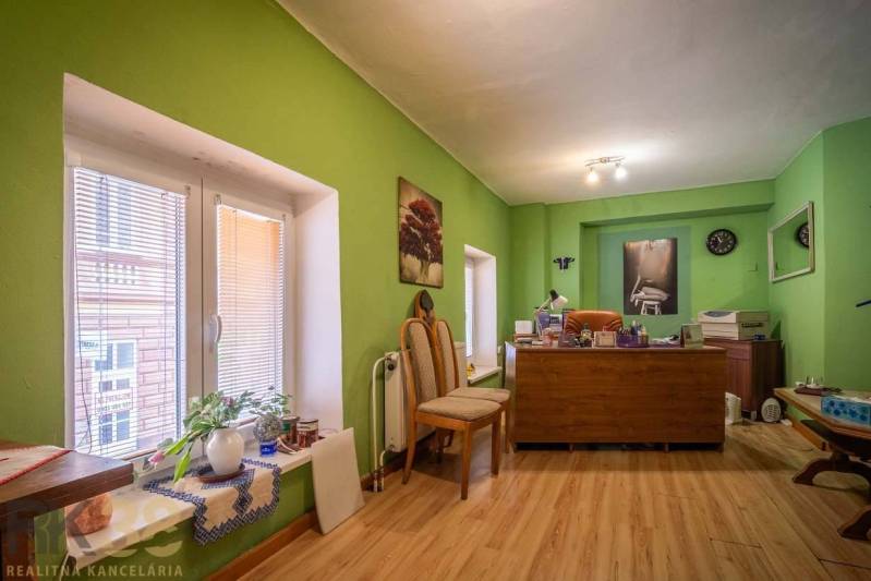 Kancelář s dřevěným dekorem podlahy, zelené stěny, pracovní stůl a dekorace.