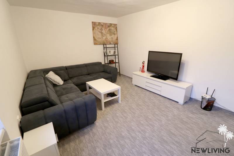 Obývací pokoj v rodinném domě s velkou sedačkou, televizí a malým stolkem.