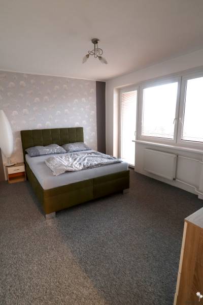 Ložnice v rodinném domě s čalouněnou postelí a šedým kobercem.