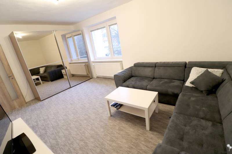 Obývací pokoj v rodinném domě s rohovou sedačkou, zrcadlová skříň, okna, koberec.