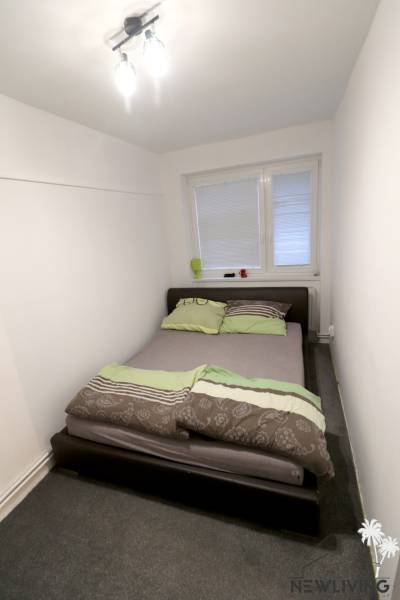 Ložnice s postelí v rodinném domě, bílé stěny, koberec.