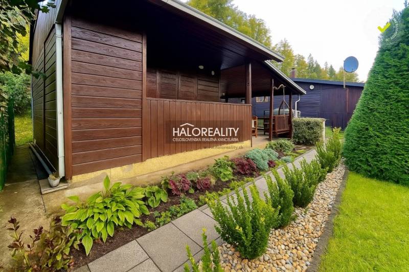 Dřevěná chatka v zahradách v Bytči, obklopená udržovanou zelení a chodníkem z dlaždic.