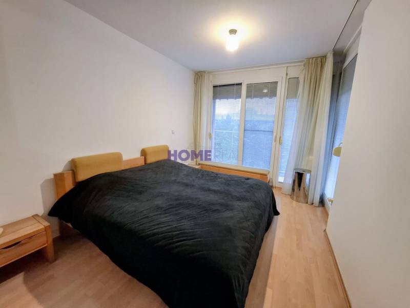 Ložnice v 2-pokojovém bytě s podlahou s dřevěným dekorem a velkými okny.