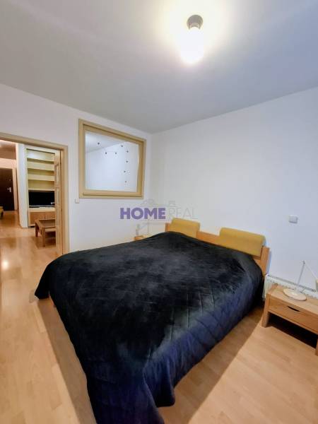 Ložnice se širokou postelí, nočními stolky a podlahou s dřevěným dekorem v dvoupokojovém bytě.