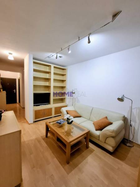 Obývací pokoj v 2-pokojovém bytě s krémovou sedačkou a podlahou s dřevěným dekorem.