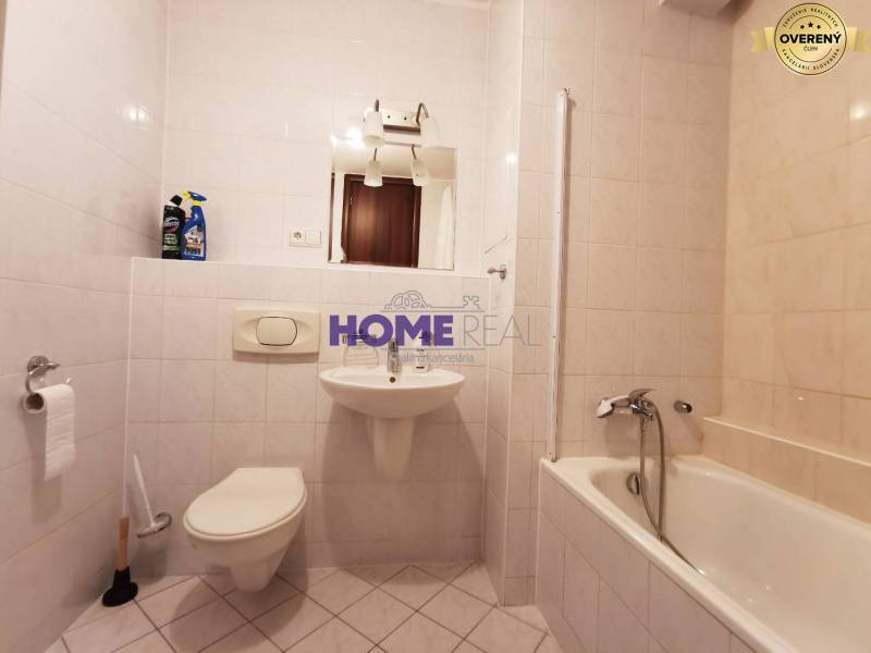 Koupelna v 2-pokojovém bytě s vanou, umyvadlem a toaletou, obložená bílými dlaždicemi.