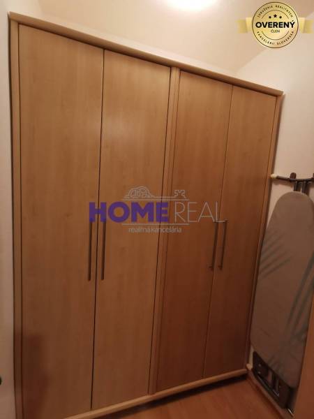 V 2-pokojovém bytě je vidět skříň s dřevěným dekorem a žehlicí prkno.