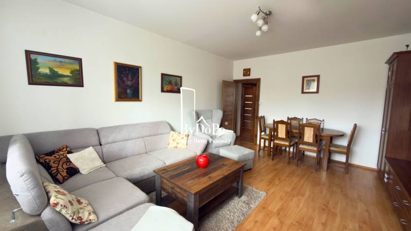 Obývací pokoj v 3-pokojovém bytě s rohovou sedačkou a podlahou s dřevěným dekorem.