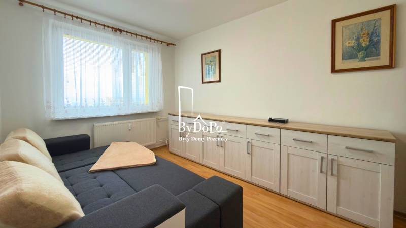 Pokoj s pohovkou, nábytkem a podlahou s dřevěným dekorem ve 3pokojovém bytě.