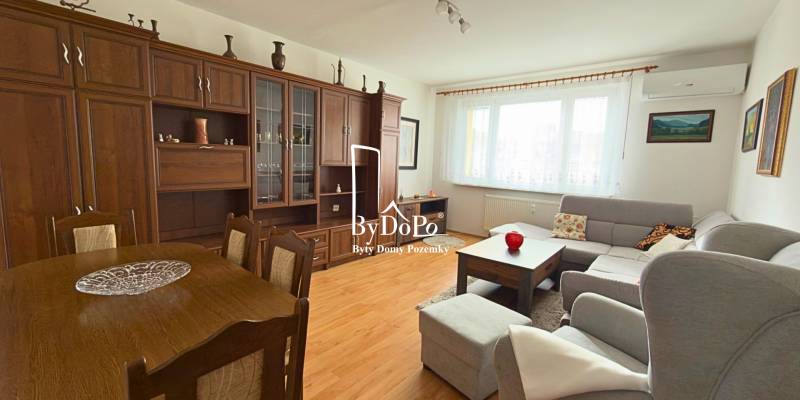 Obývací pokoj v 3-pokojovém bytě s podlahou s dřevěným dekorem a velkou sedací soupravou.