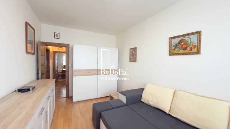 Obývací pokoj s pohovkou, skříní a podlahou s dřevěným dekorem ve 3pokojovém bytě.