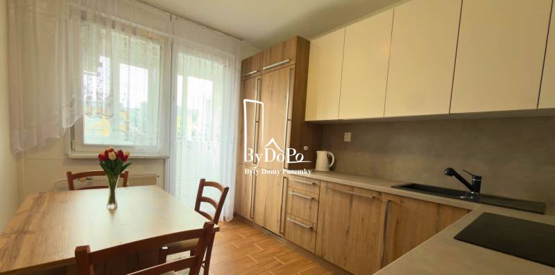 Kuchyně v 3-pokojovém bytě s dřevěným dekorem a světlým nábytkem, elegantní květiny na stole.