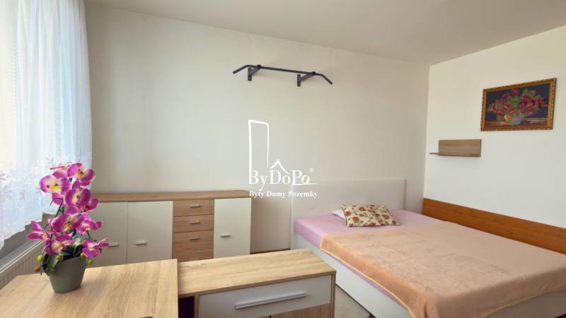 Ložnice s postelí, skříní a dekorativními květinami v 3-pokojovém bytě.