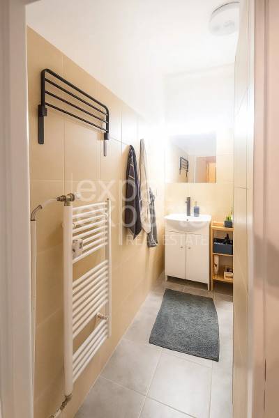 Koupelna ve 3-pokojovém bytě se světlými obklady, umyvadlem a žebříkovým radiátorem.