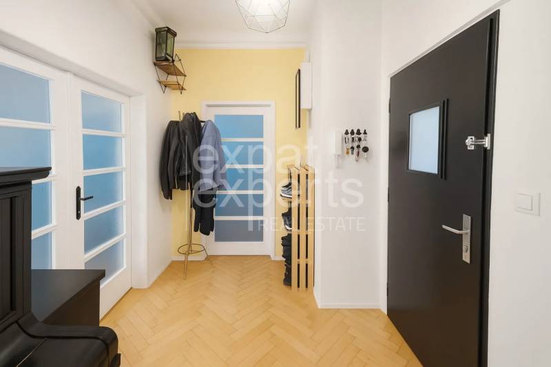 Chodba v 3-pokojovém bytě s podlahou s dřevěným dekorem, věšákem a dveřmi.