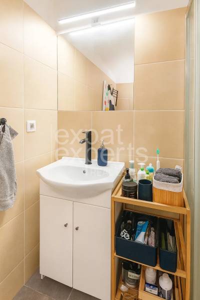 Koupelna s umyvadlem, úložným prostorem a světlou dlažbou v 3-pokojovém bytě.