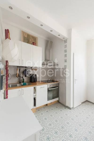 Kuchyně v 3-pokojovém bytě s dlažbou, bílými skříňkami a dřevěným dekorem pultu.