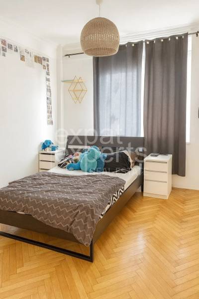 Ložnice s postelí, nočními stolky a podlahou s dřevěným dekorem ve 3pokojovém bytě.