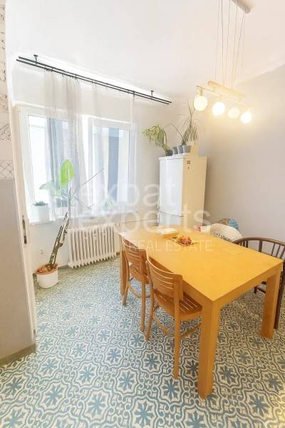 Jídelní kout ve 3-pokojovém bytě s dřevěným stolem a vzorovanou podlahou.