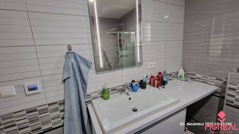 Koupelna v rodinném domě s umyvadlem, zrcadlem s osvětlením a sprchovým koutem.