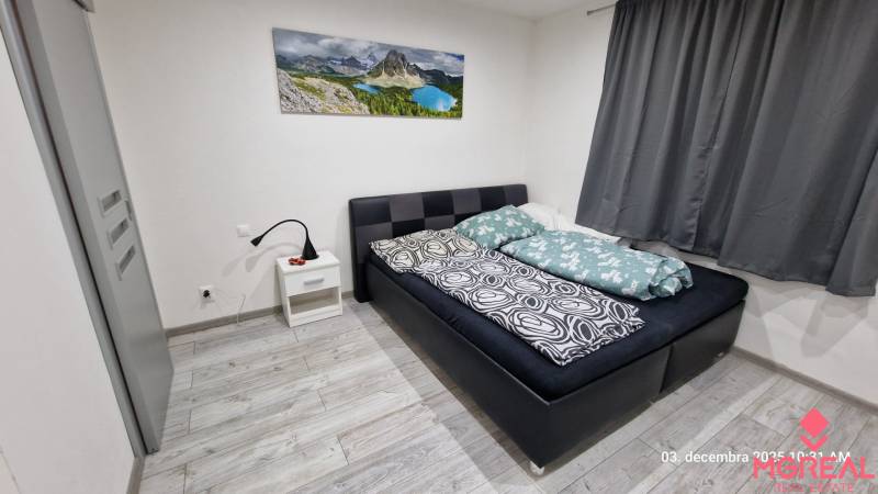 Ložnice v rodinném domě s postelí, nočním stolkem a podlahou s dřevěným dekorem.