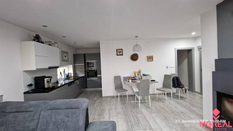 Interiér rodinného domu s kuchyní, jídelním stolem a podlahou s dřevěným dekorem.