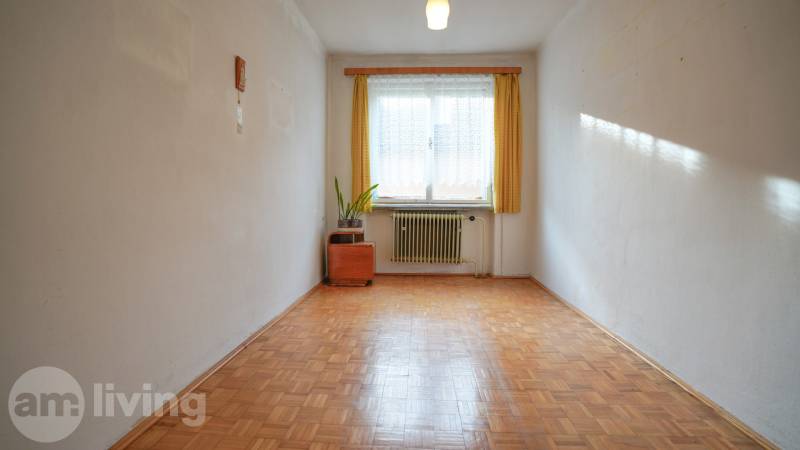 Pokoj v rodinném domě s podlahou s dřevěným dekorem, radiátorem a oknem se záclonou.