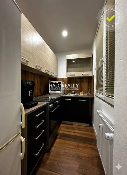 Kuchyně v 1-pokojovém bytě s podlahou s dřevěným dekorem a tmavými skříňkami.