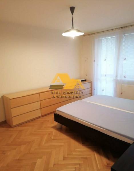 Ložnice v 3-pokojovém bytě s postelí a komodou na podlaze s dřevěným dekorem.