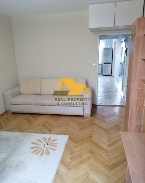 Obývací pokoj ve 3pokojovém bytě s podlahou s dřevěným dekorem a světlou sedačkou.