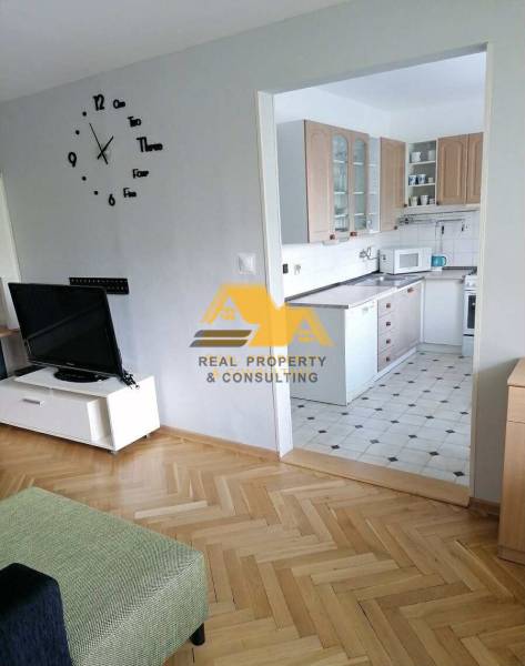 Obývací pokoj v 3-pokojovém bytě s podlahou s dřevěným dekorem a kuchyní v pozadí.