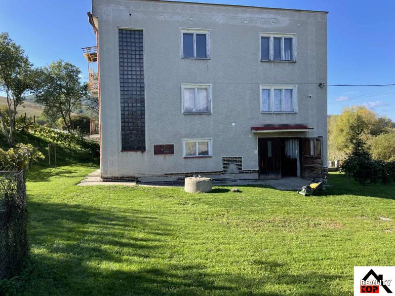 Rodinný dům v Hajnáčce s trávníkem, stromy a zahradním nářadím na dvoře.